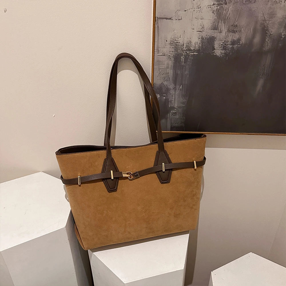 Brown handbag with black accents on a white surface with abstract art in the background