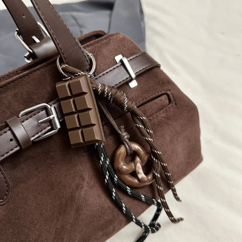 Brown handbag with decorative elements including a chocolate bar and knotted rope on a blurred background.