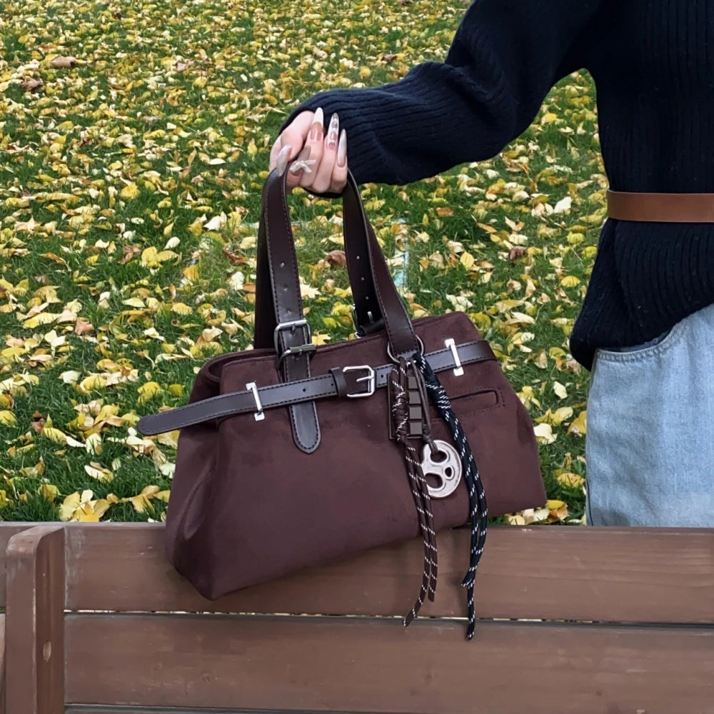 Brown handbag with decorative straps on a wooden bench against a grassy background