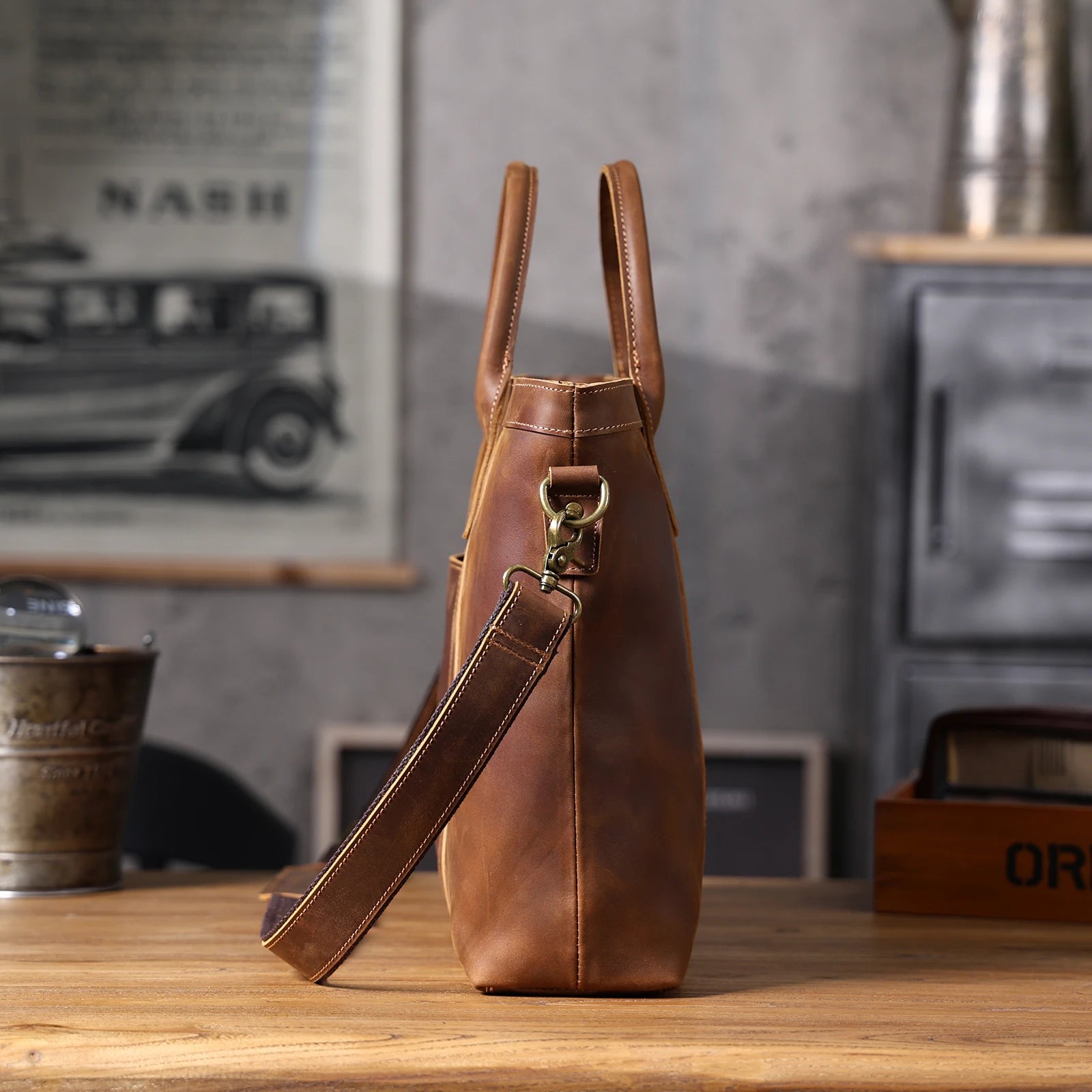 Brown leather bag on a wooden surface with a vintage car poster in the background