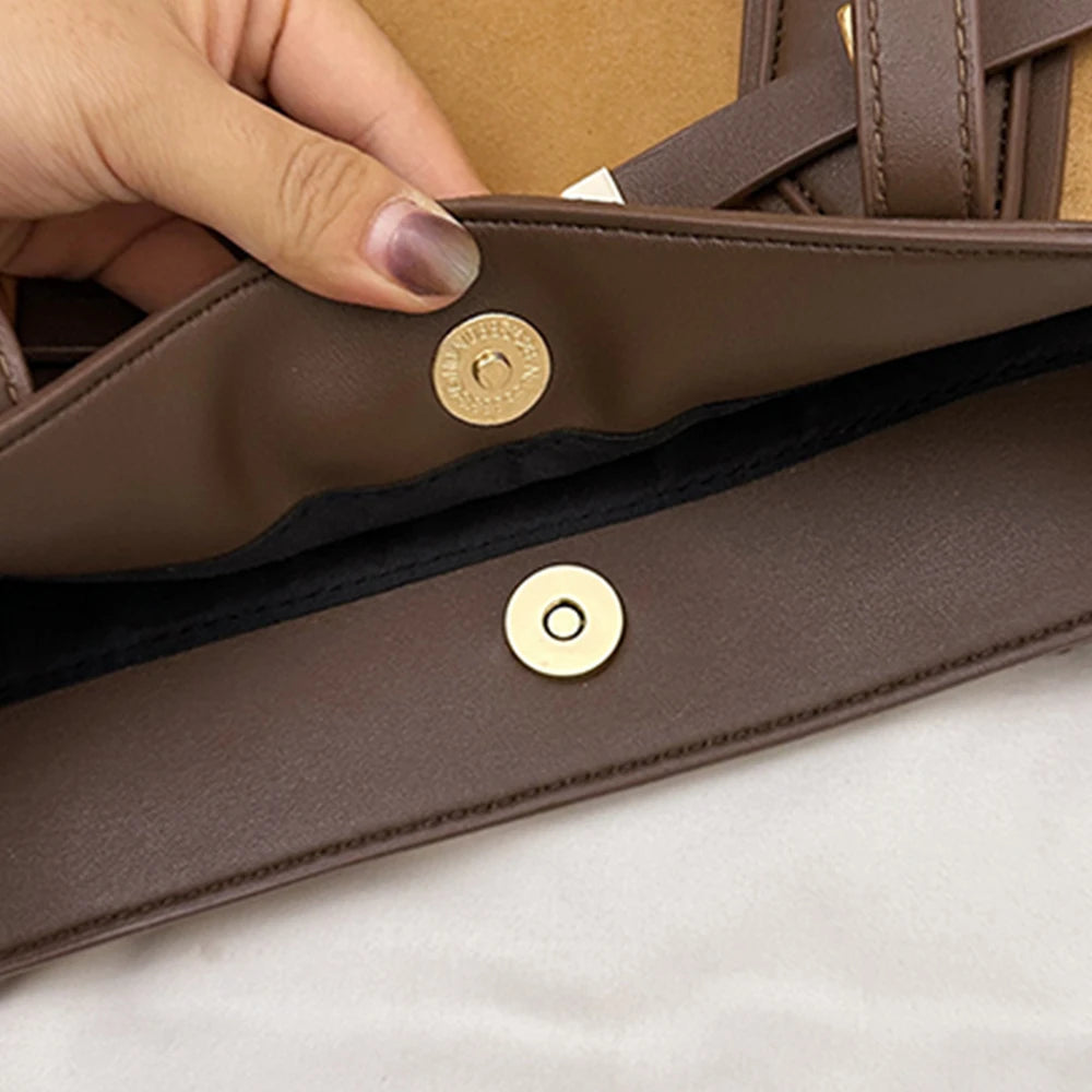 Brown leather bag with gold buttons held by a hand on a light background