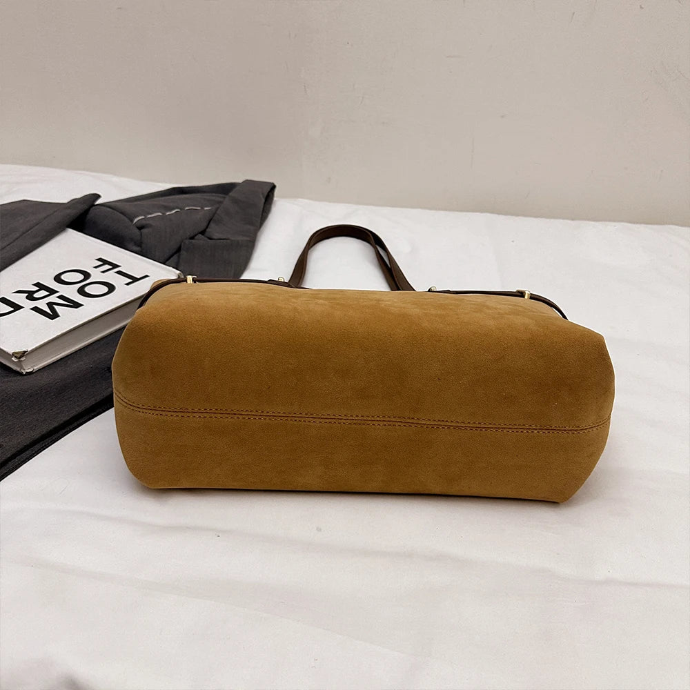 Brown leather duffel bag on a white surface with a magazine and gray jacket in the background.