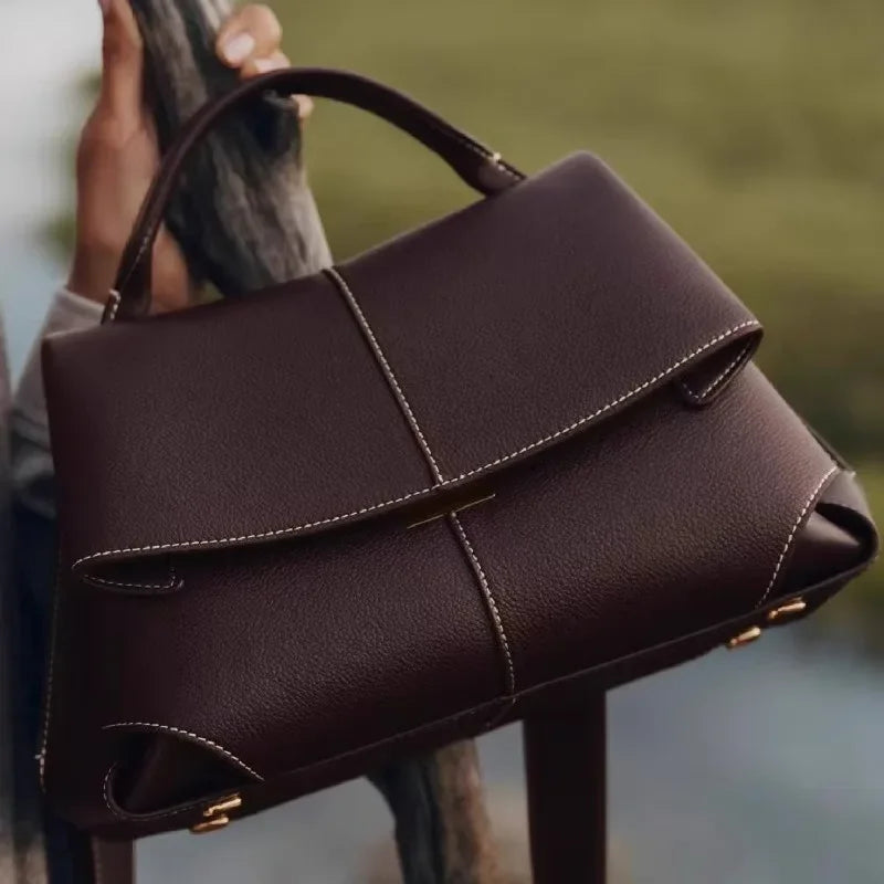 Brown leather handbag held by a person with a blurred background