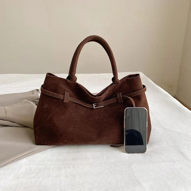 Brown leather handbag with a smartphone on a white surface