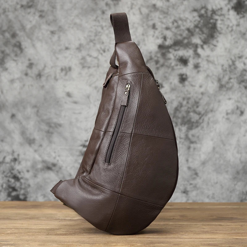 Brown leather sling bag on a wooden surface with a gray textured background