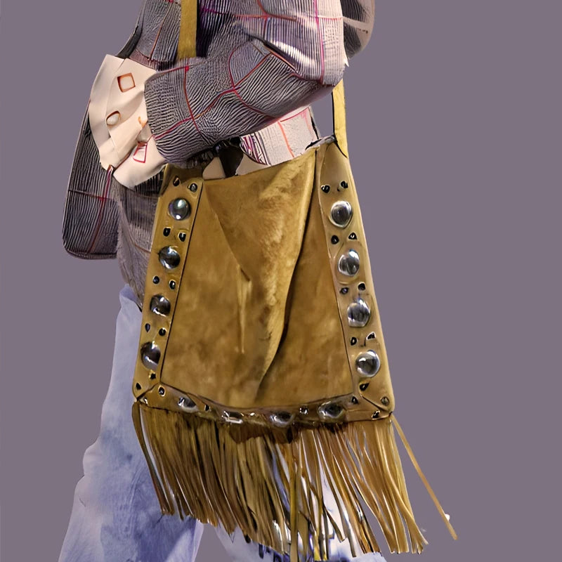 Brown suede bag with fringe and studs held by a person against a gray background