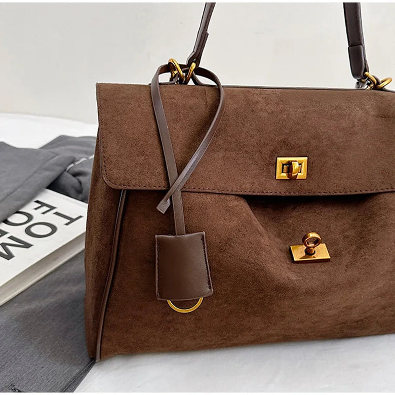 Brown suede handbag with gold hardware on a light gray surface