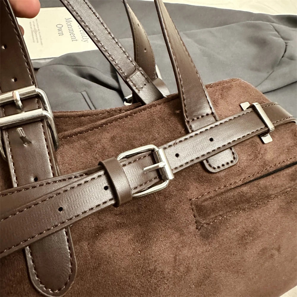 Brown suede handbag with leather straps and buckle on a blurred background