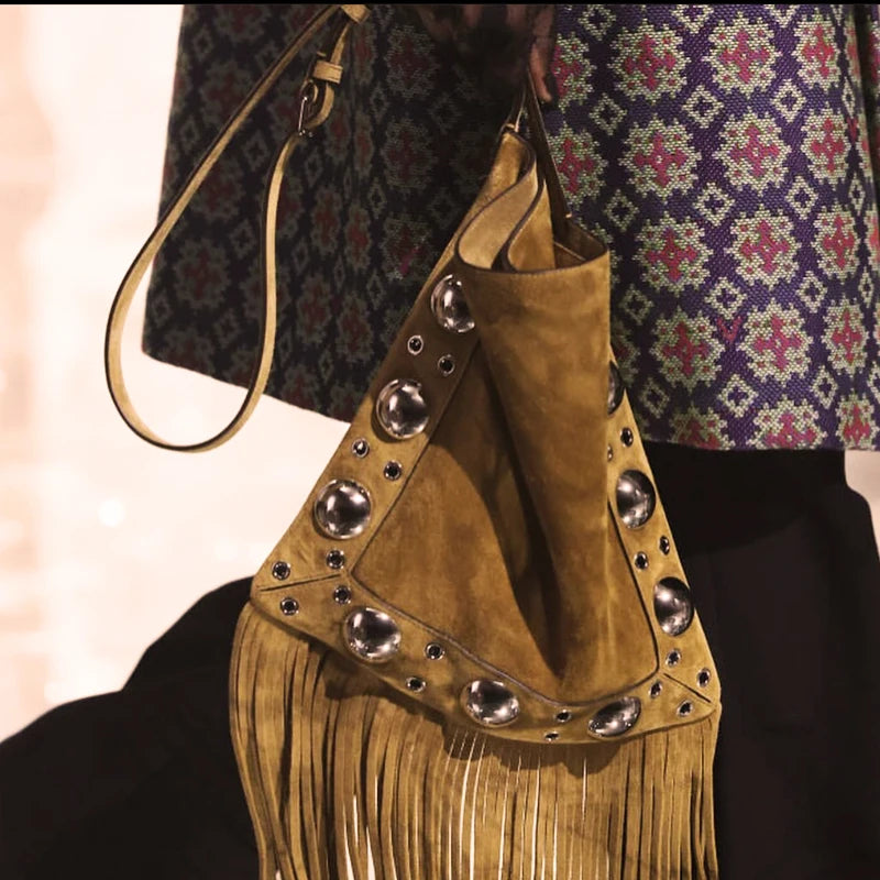 Brown suede handbag with silver studs and fringes held by a person wearing a patterned garment.