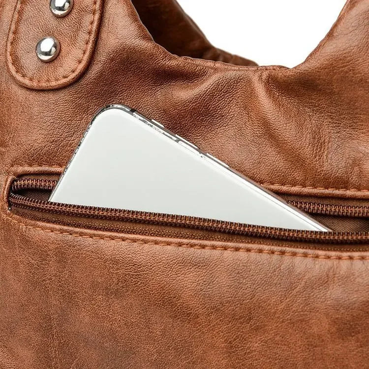 Close-up of a brown leather bag with a silver phone inside a pocket.
