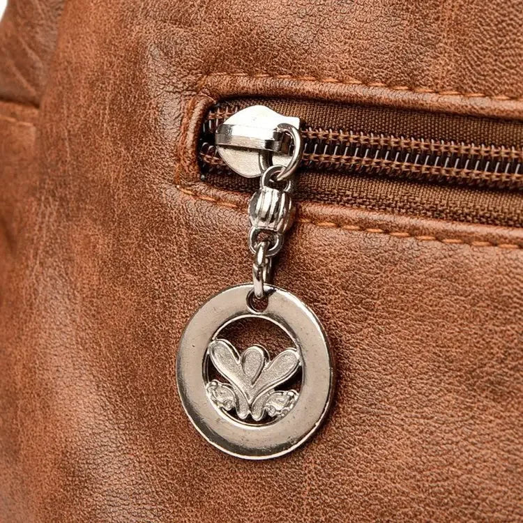 Close-up of a brown leather bag with a silver zipper and decorative pendant.