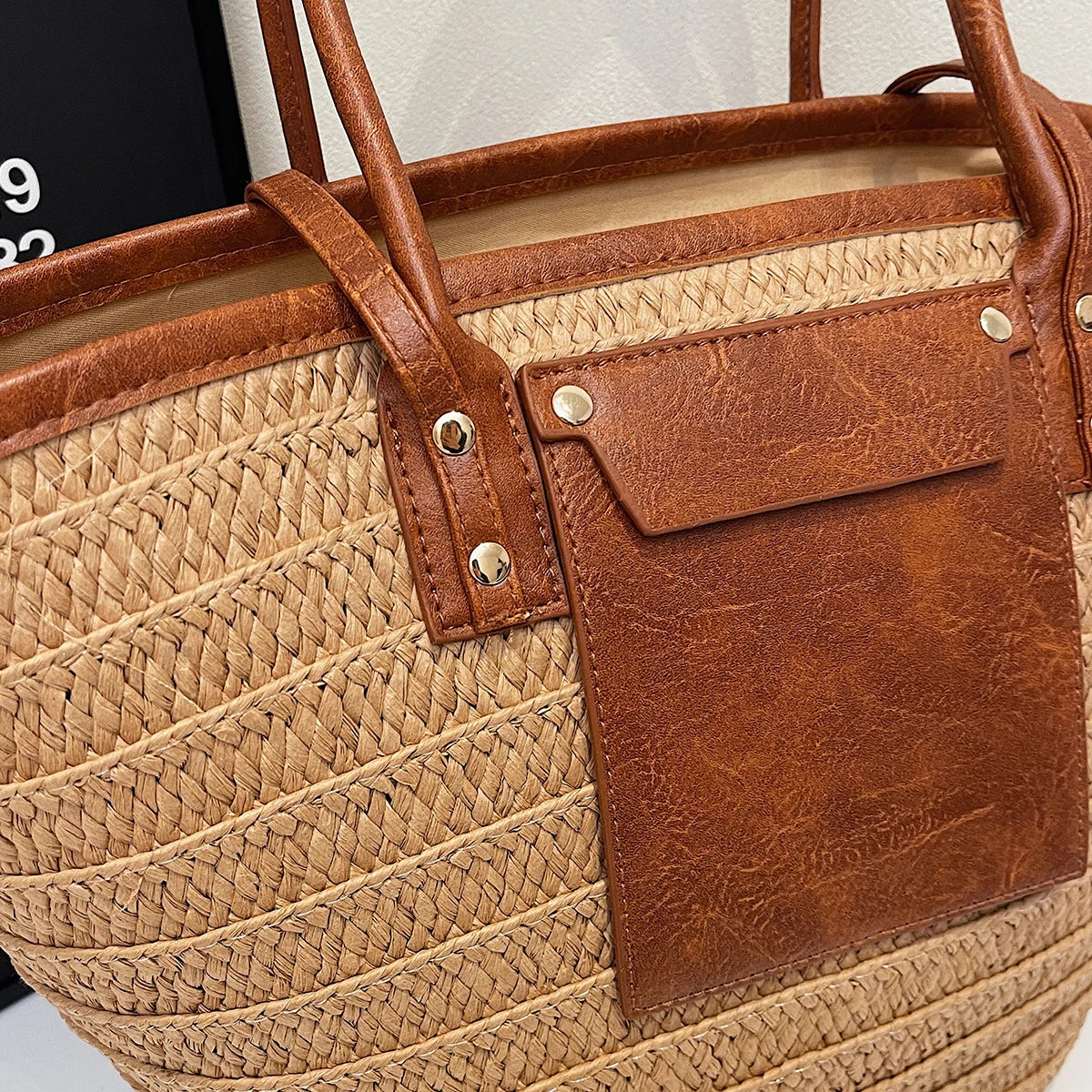 Close-up of a straw bag with brown leather accents and visible brand name.