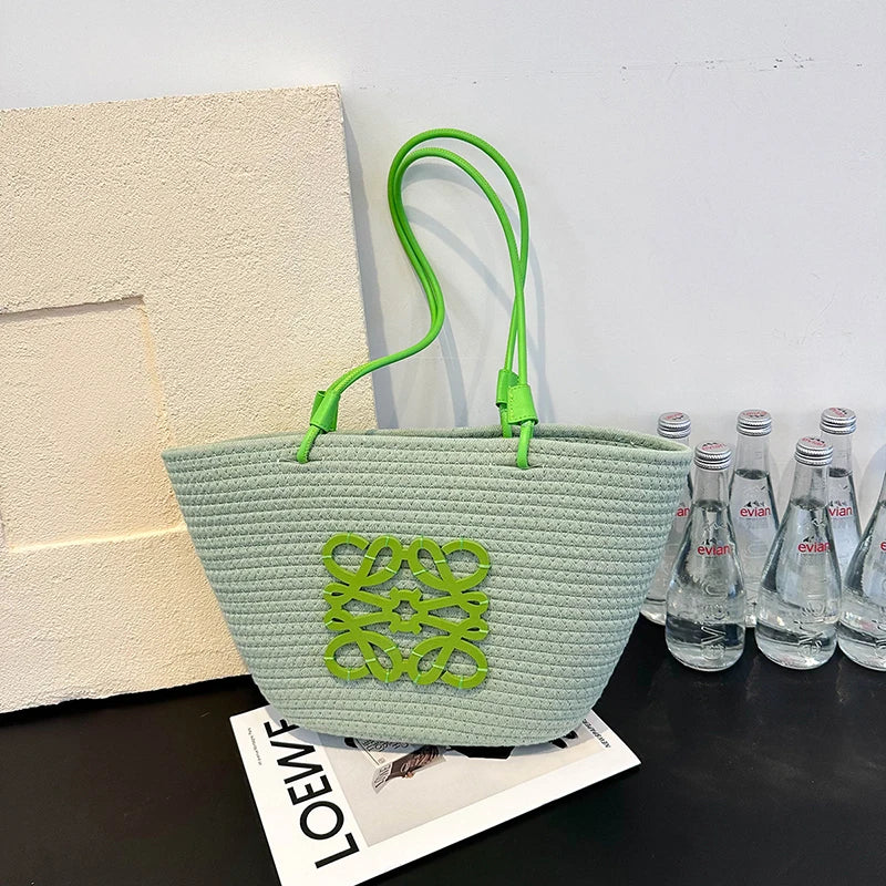 Light green woven bag with green handle and logo on a surface with water bottles in the background.
