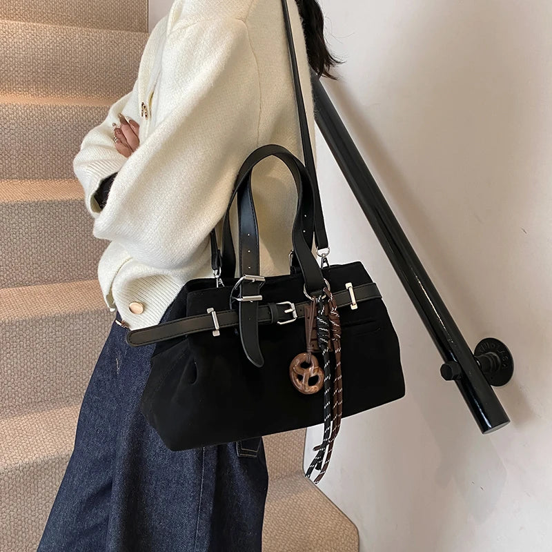 Person holding a black handbag with a strap against a neutral wall.