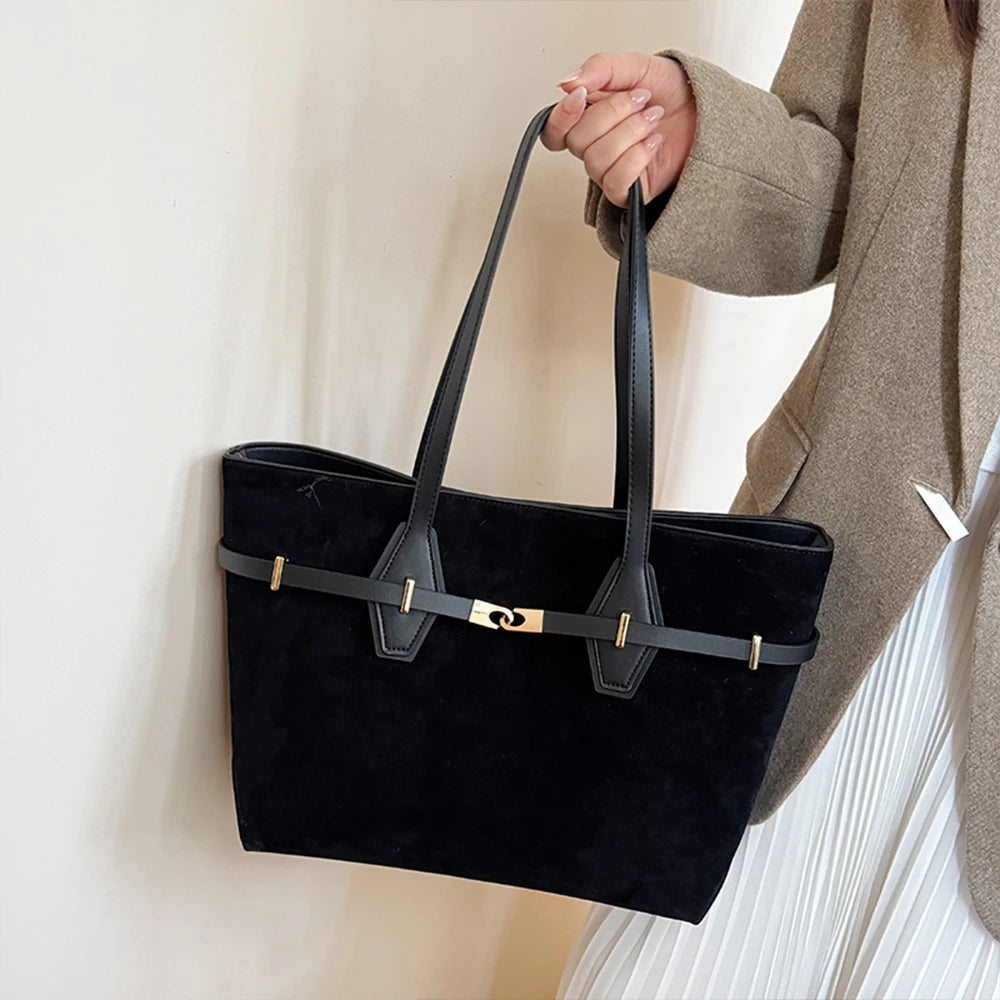 Person holding a black handbag with gold accents against a neutral background