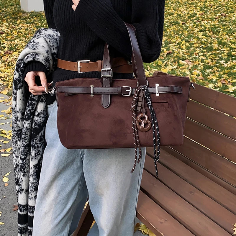 Person holding a brown handbag with a decorative strap on a bench outdoors.