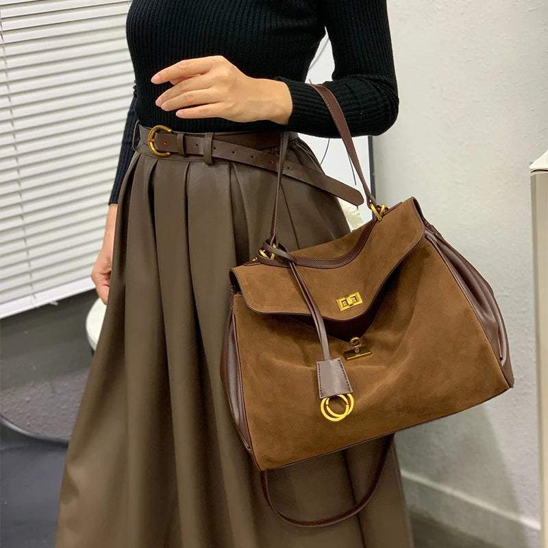 Person holding a brown handbag with a gold clasp in an indoor setting