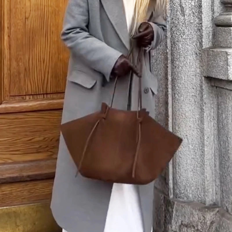 Person holding a brown leather bag against a building background