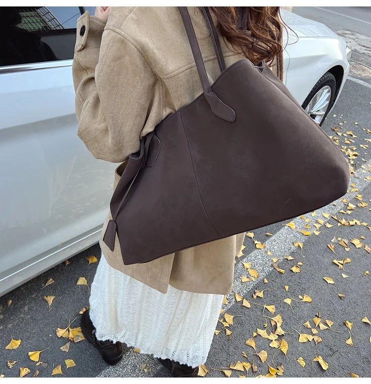 Person holding a brown leather handbag on a street with fallen leaves.