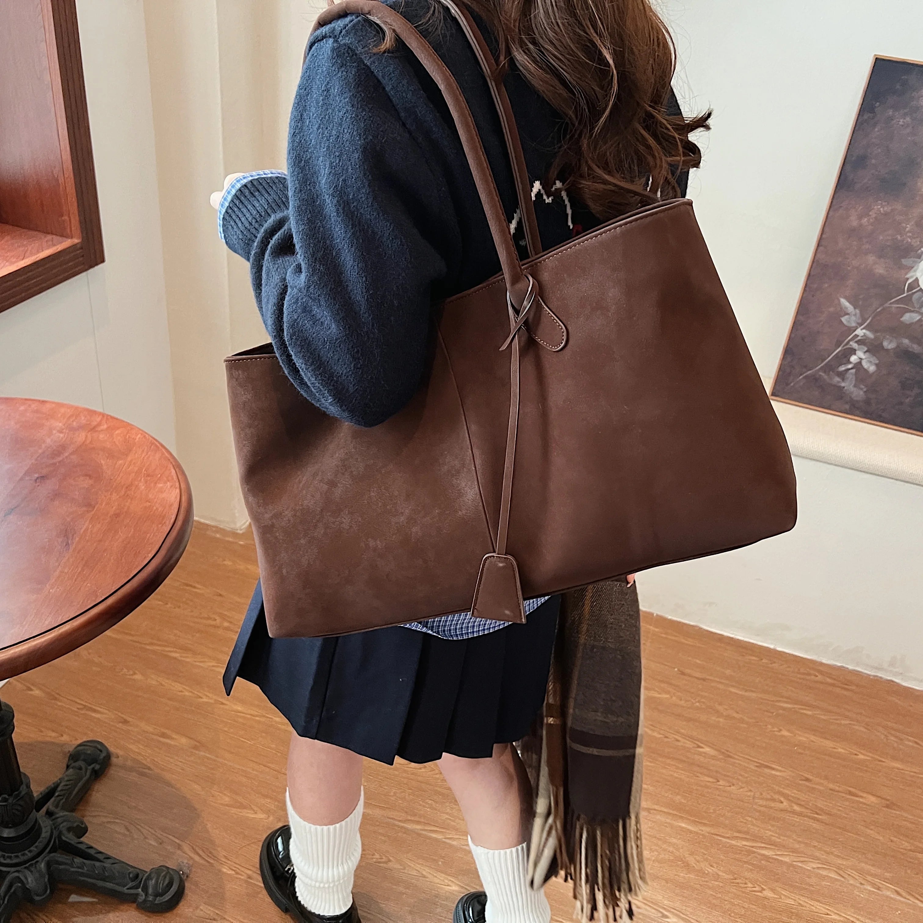 Person holding a brown leather tote bag in an indoor setting