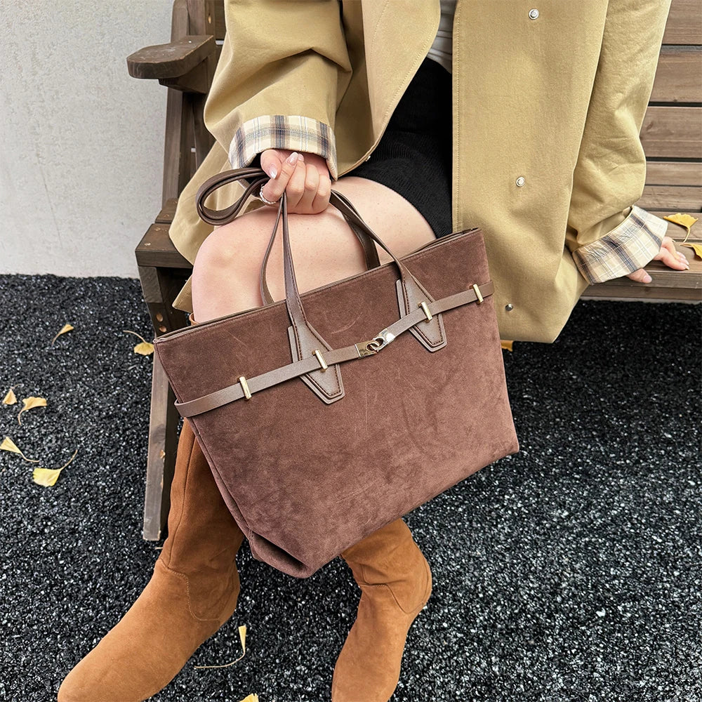 Person holding a brown suede handbag with a matching coat and boots on a bench.