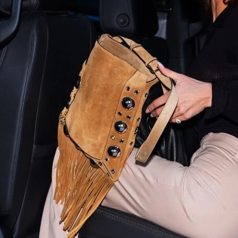 Person holding a brown suede handbag with fringe and studs in a car.