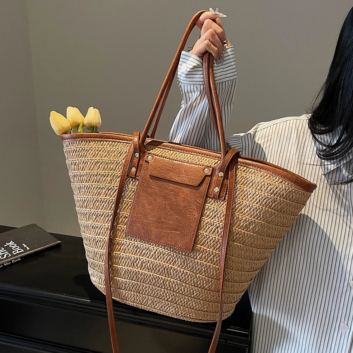 Person holding a straw handbag with a brown leather patch