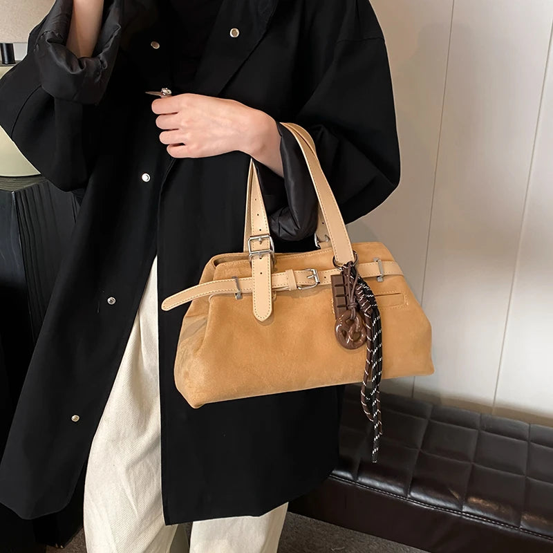 Person holding a tan handbag with a black coat and white pants.