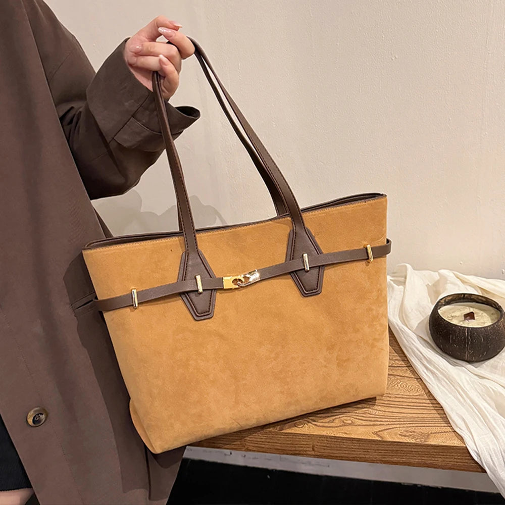 Person holding a tan handbag with brown straps on a wooden surface.