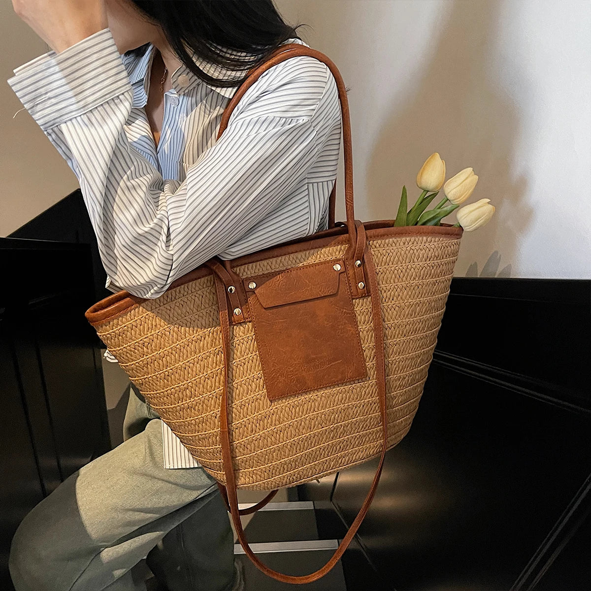 Person holding a woven handbag with a floral arrangement, sitting on a chair.