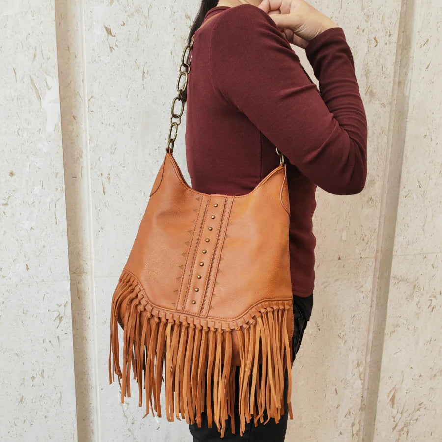 Person wearing a brown leather handbag with fringe details against a light background