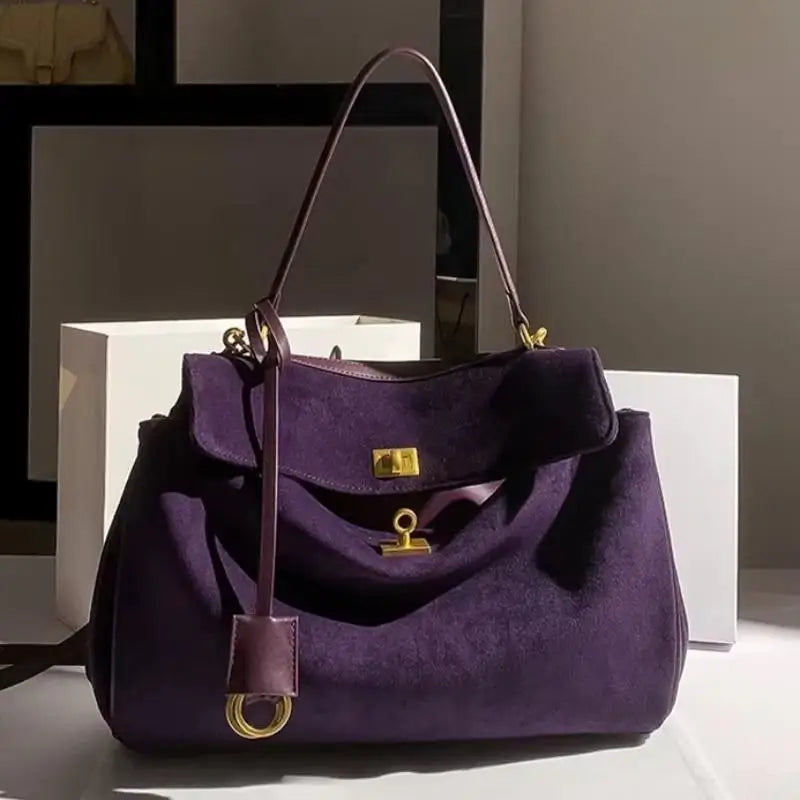 Purple handbag with gold accents on a white surface