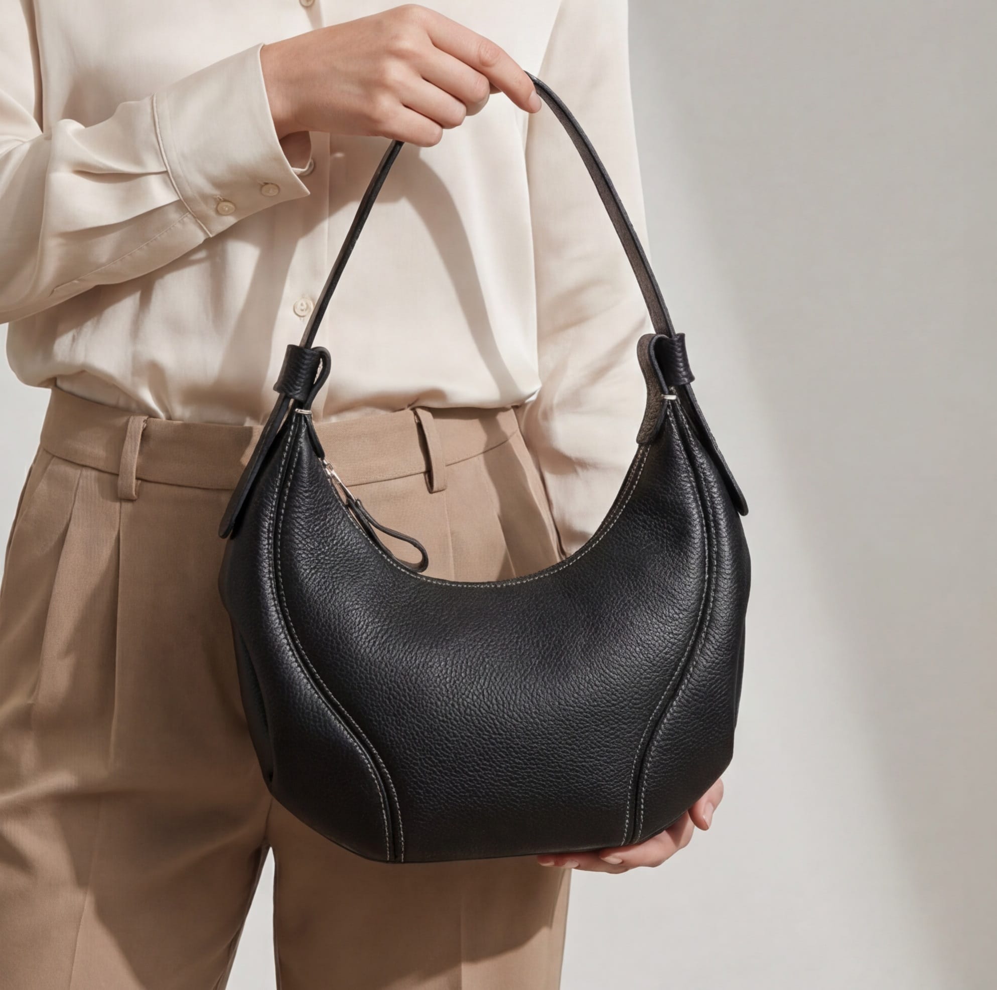 Person holding a black handbag against a neutral background