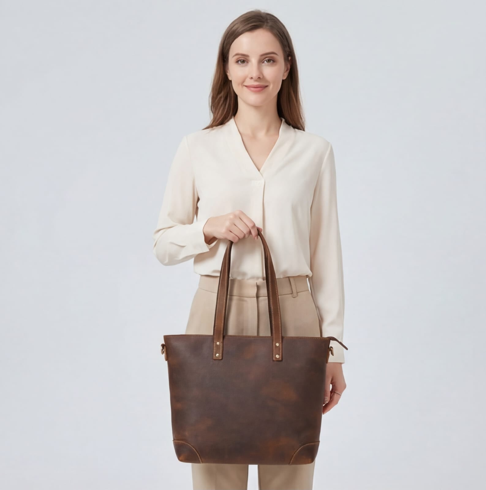 Woman holding a brown leather tote bag against a plain background