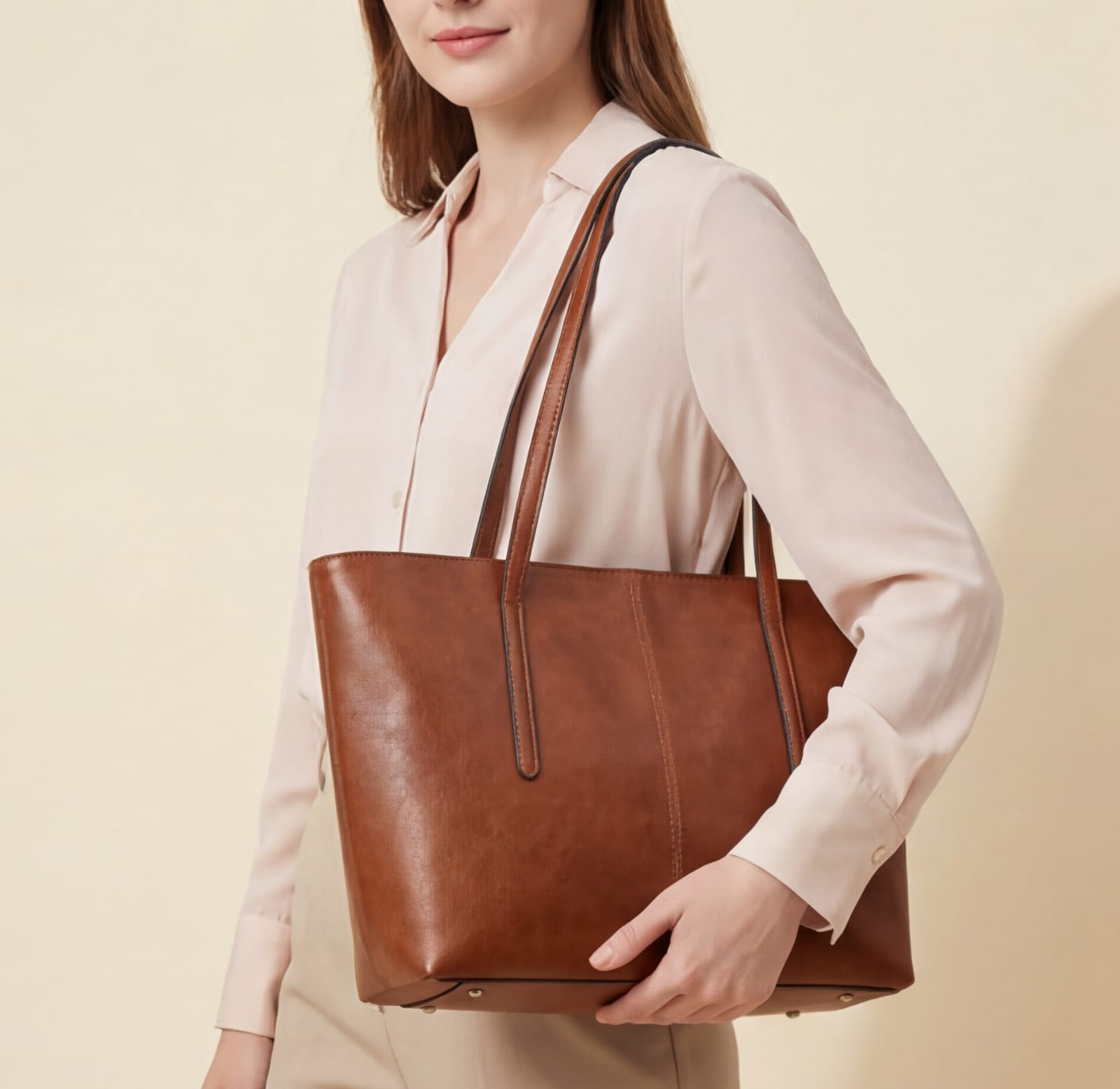 Woman holding a brown leather tote bag against a beige background