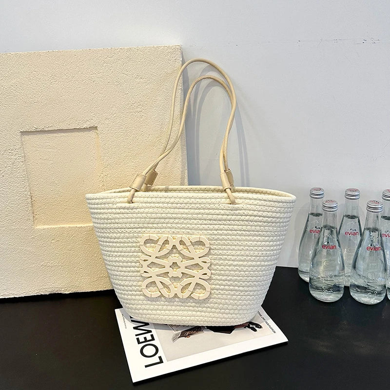 White woven handbag with a decorative logo on a black surface with water bottles in the background.