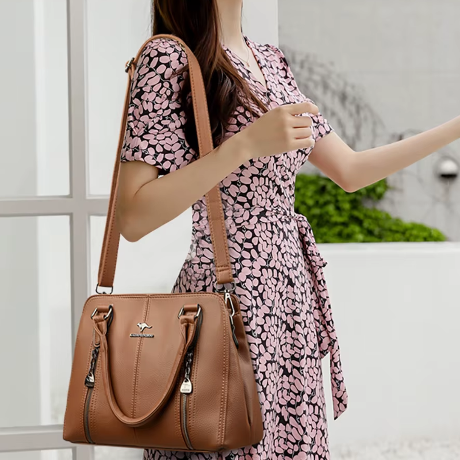 Woman holding a brown handbag with a floral dress in an outdoor setting