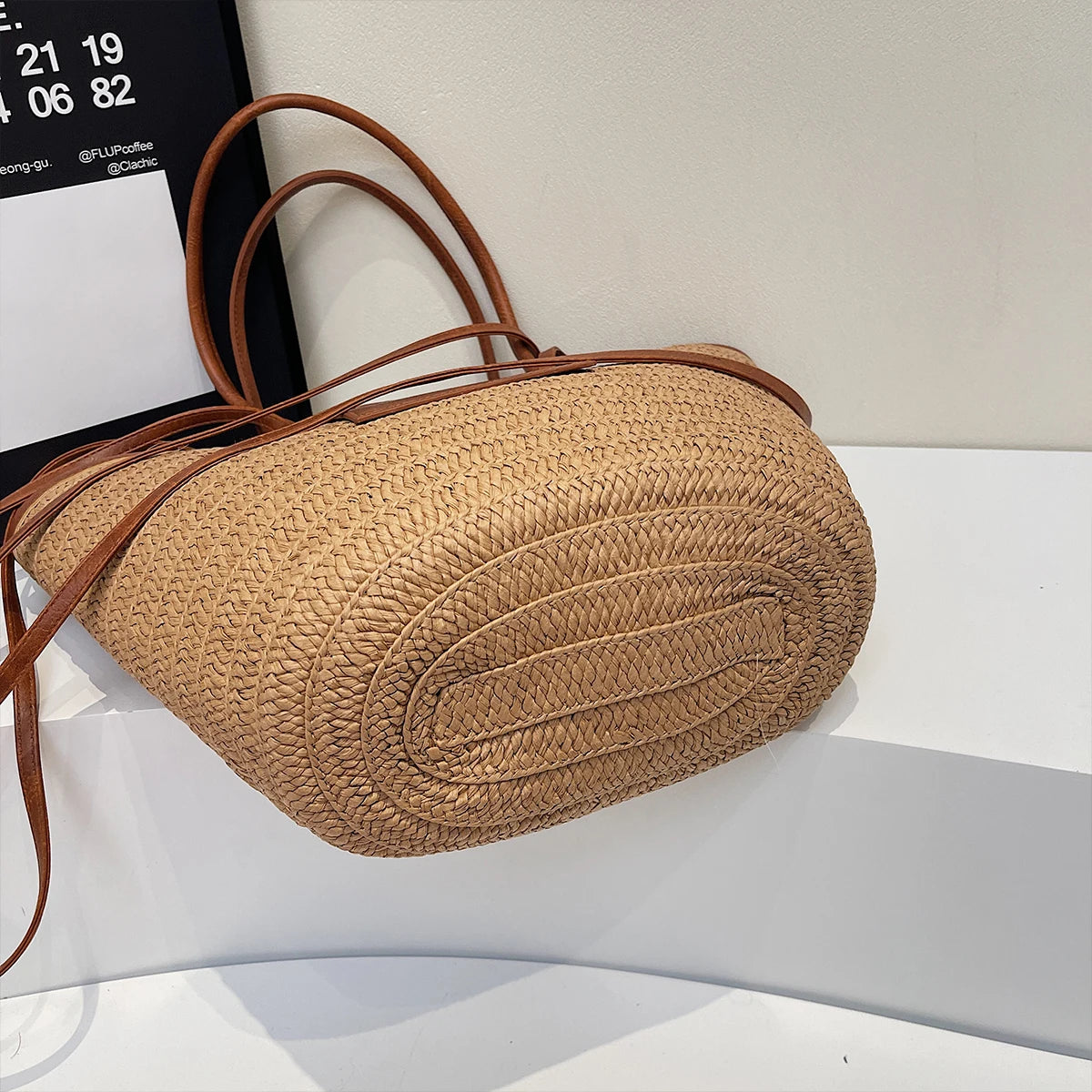 Woven handbag with brown leather straps on a white surface