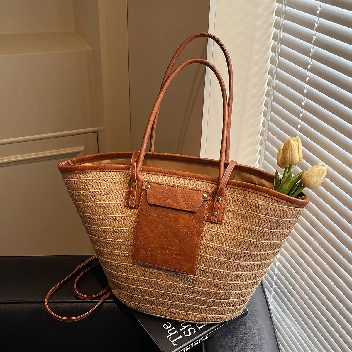 Woven handbag with leather accents on a surface near a window with blinds.