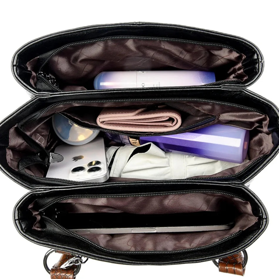 Interior view of a black leather handbag showcasing multiple compartments filled with essentials like a phone, wallet, cosmetics, and a tablet