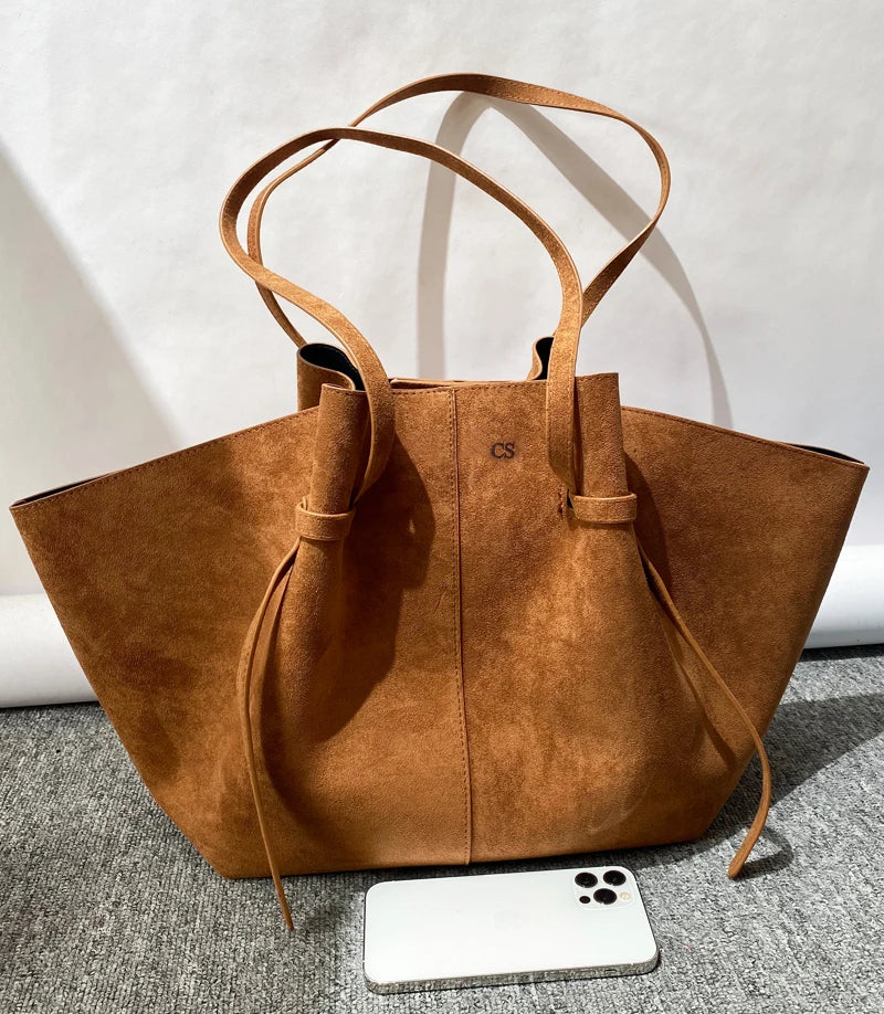 brown suede tote bag with long handles standing on carpet with smartphone for scale, front view