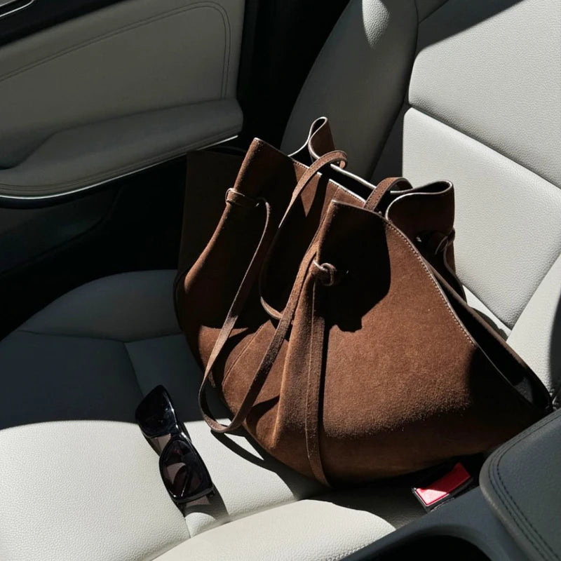 brown suede tote bag placed on car seat with sunlight and sunglasses beside it